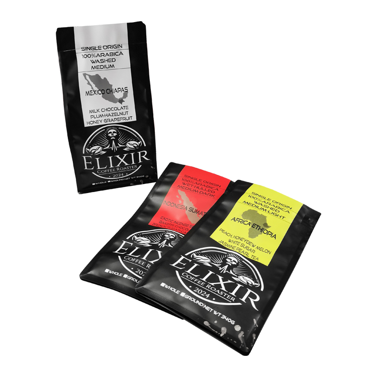 White-label black coffee bag upright beside red and yellow label bags